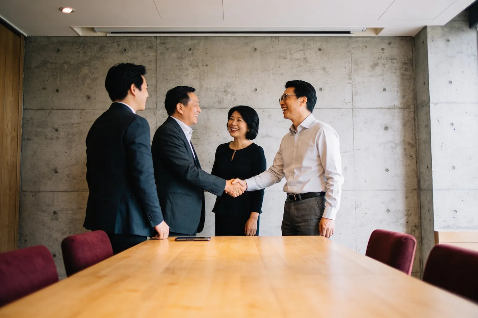 例會開始前的包廂裡,一位成員把兩個人介紹給彼此,兩人正在握手,旁邊的人笑著看。