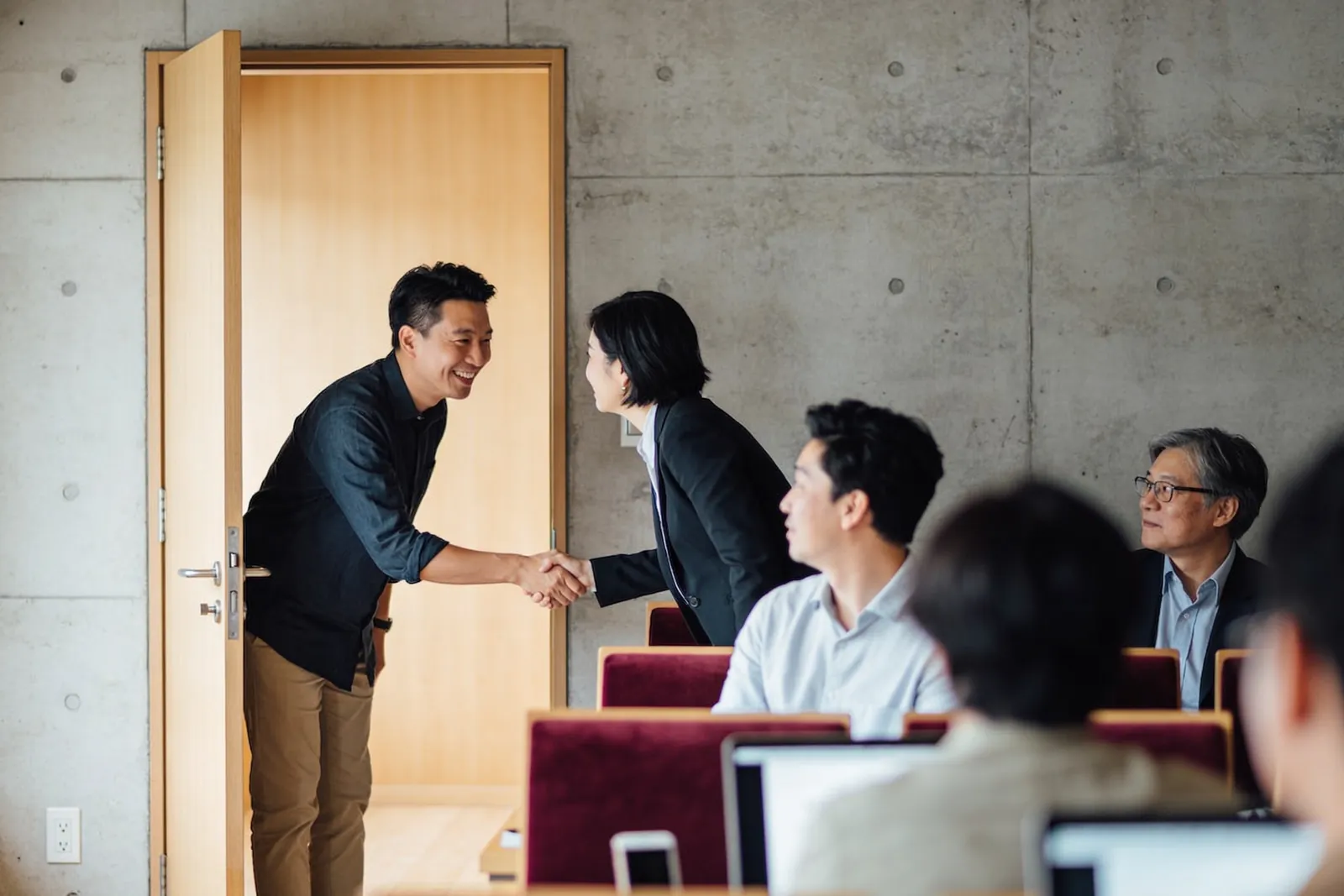 另一堂課開始前，講師在教室門口笑著跟學員握手，其他人已經坐下。